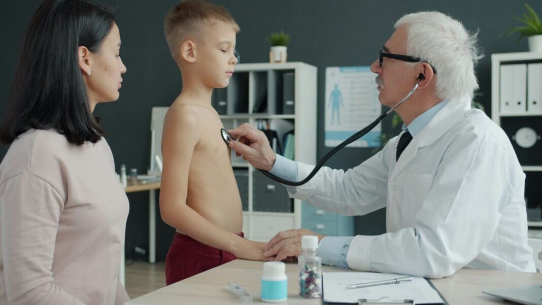 A doctor examines a young boy's chest with a stethoscope while his mother watches