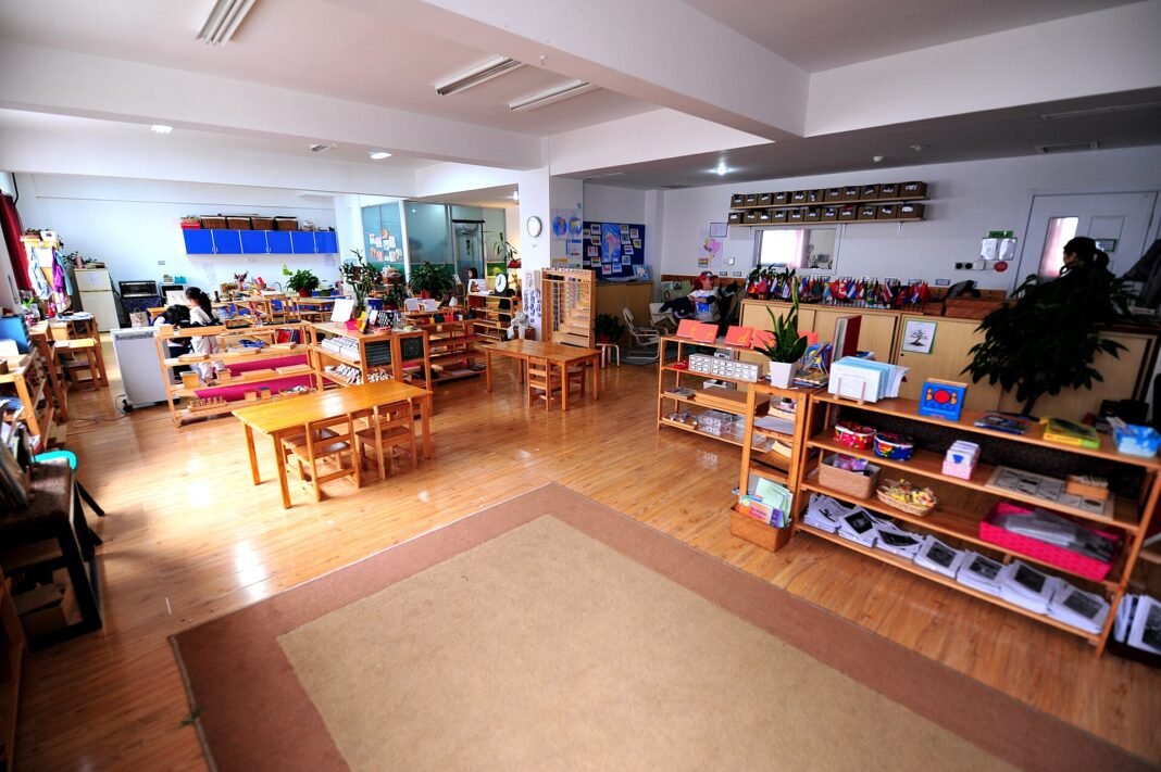 A bright international school early-years classroom with wooden tables and learning materials on shelves